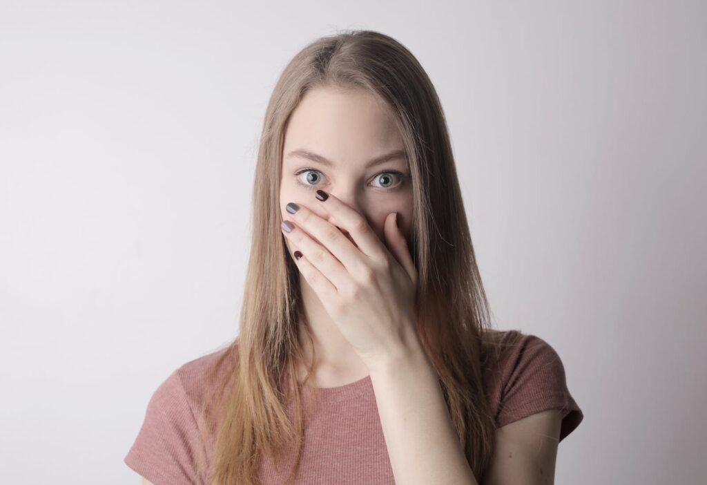 Young amazed woman in casual wear covering mouth while keeping secret