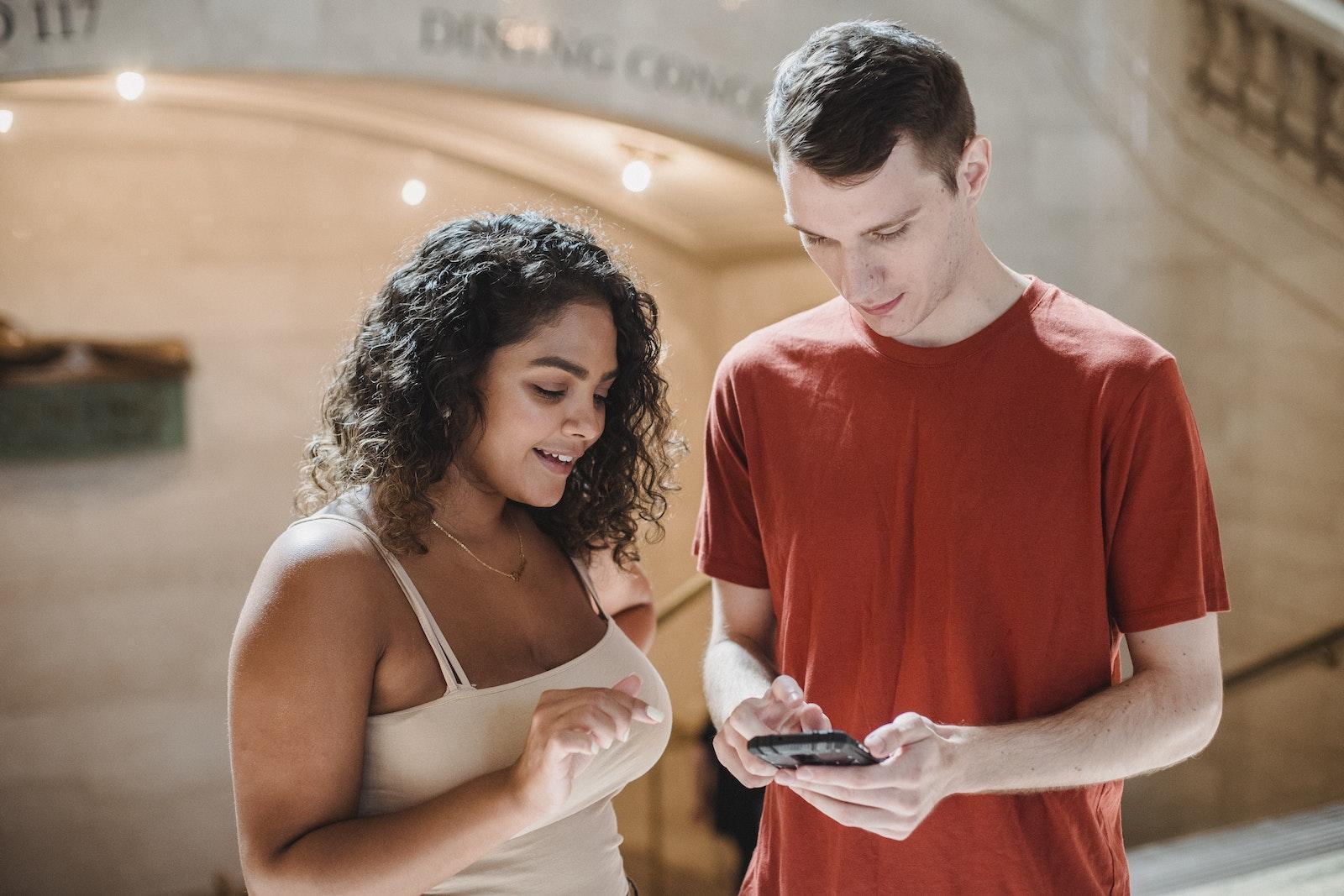 Positive young diverse students surfing smartphone in hallway