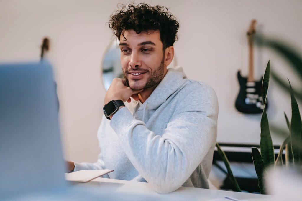 Positive freelancer sitting at table and using laptop at home