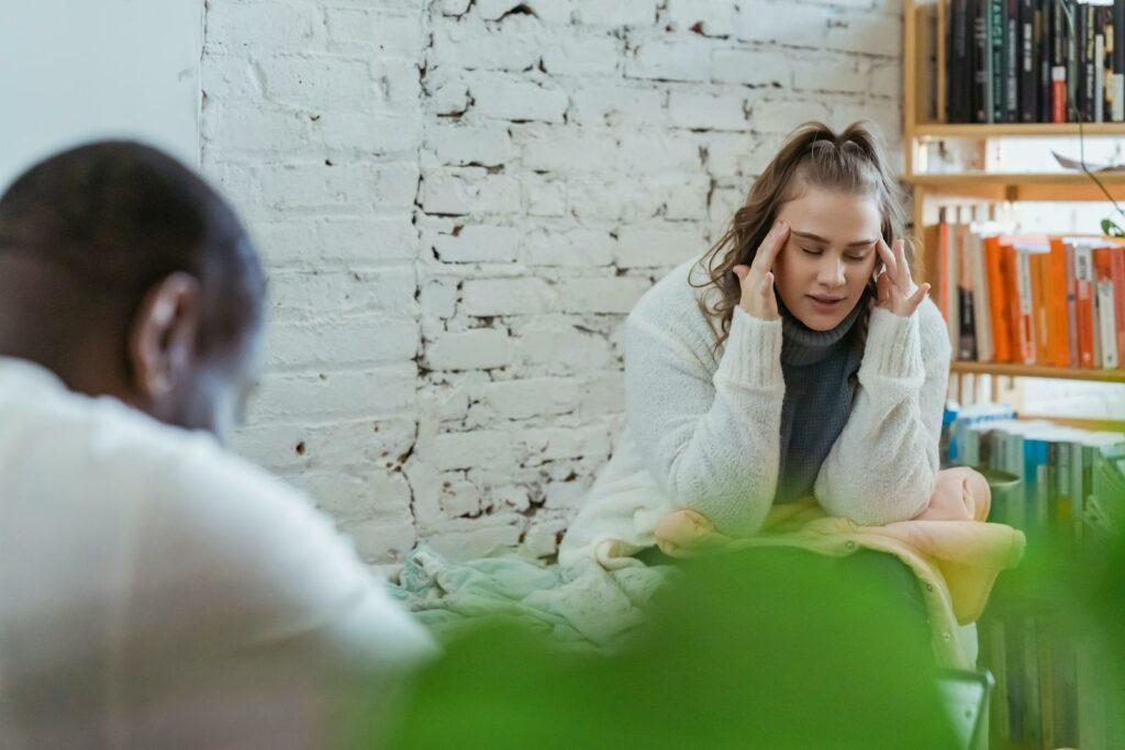 Exhausted woman calming down after argument with husband by putting fingers on temples and man sitting and looking down