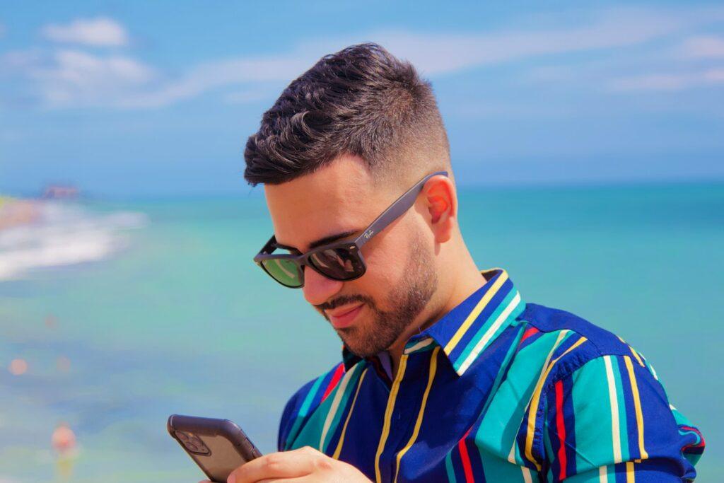 man in blue and red striped polo shirt holding black smartphone during daytime