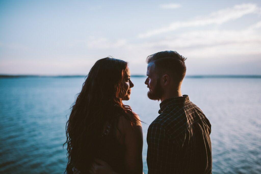 man and woman standing while looking each other near body of water
