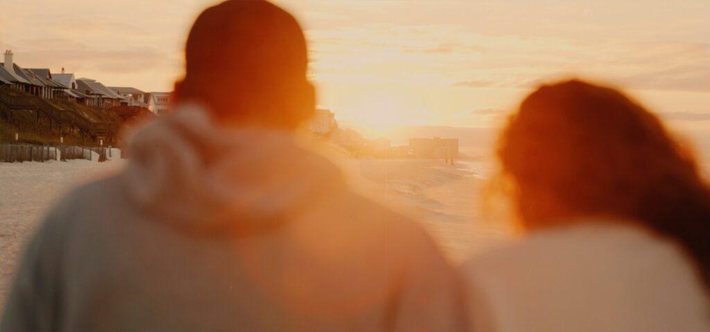 two people walking on a beach at sunset