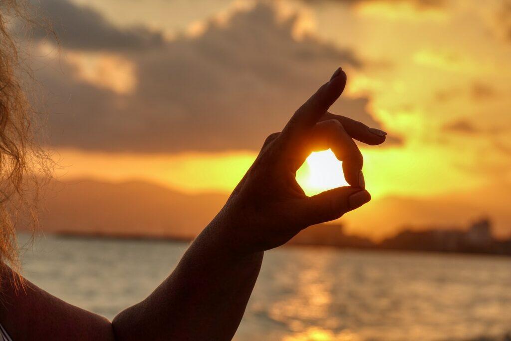a woman holding up a heart shaped object in front of a sunset