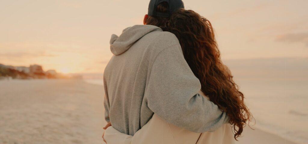 a man and woman walking on the beach at sunset